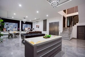A modern kitchen with a central island, a dining area with a table and chairs, and a staircase leading to an upper level. - THE I-CON Luxury PoolVilla Pattaya "10 bed" Ocean Yacht Club 4 km (Pattaya)