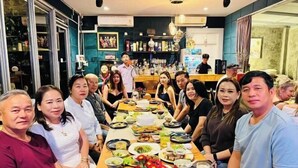 A group of people seated around a table with various dishes and drinks, in a room with a bar and shelves in the background. - 90/9 Pool Villa Chiang Mai (Chiang Mai)