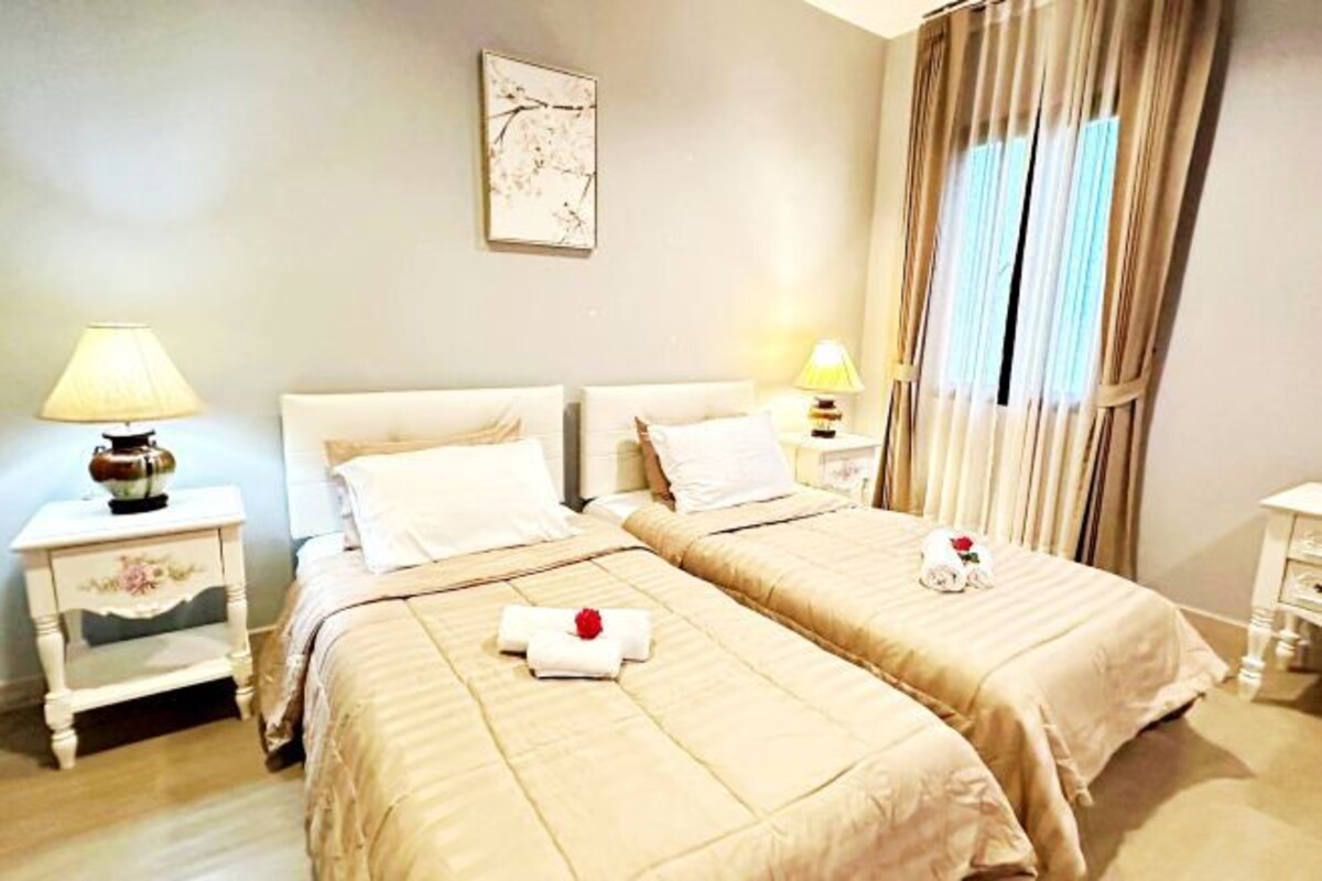 A hotel room with two beds, a nightstand with a lamp, a framed picture on the wall, and a window with curtains.