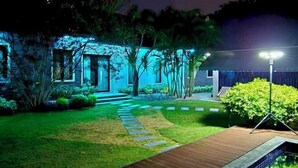 A well-lit garden pathway leading to a building with a modern design, surrounded by greenery and a wooden deck. - 90/9 Pool Villa Chiang Mai (Chiang Mai)