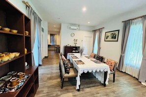 A dining area with a long table, chairs, a shelf with bowls, and a clock on the wall. - Ban 5 Rai Poollvilla (Chiang Mai)