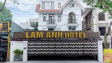 La entrada del Hotel Lam Anh, con un letrero destacado, un camino de entrada con puerta de reja y la fachada del edificio al fondo.