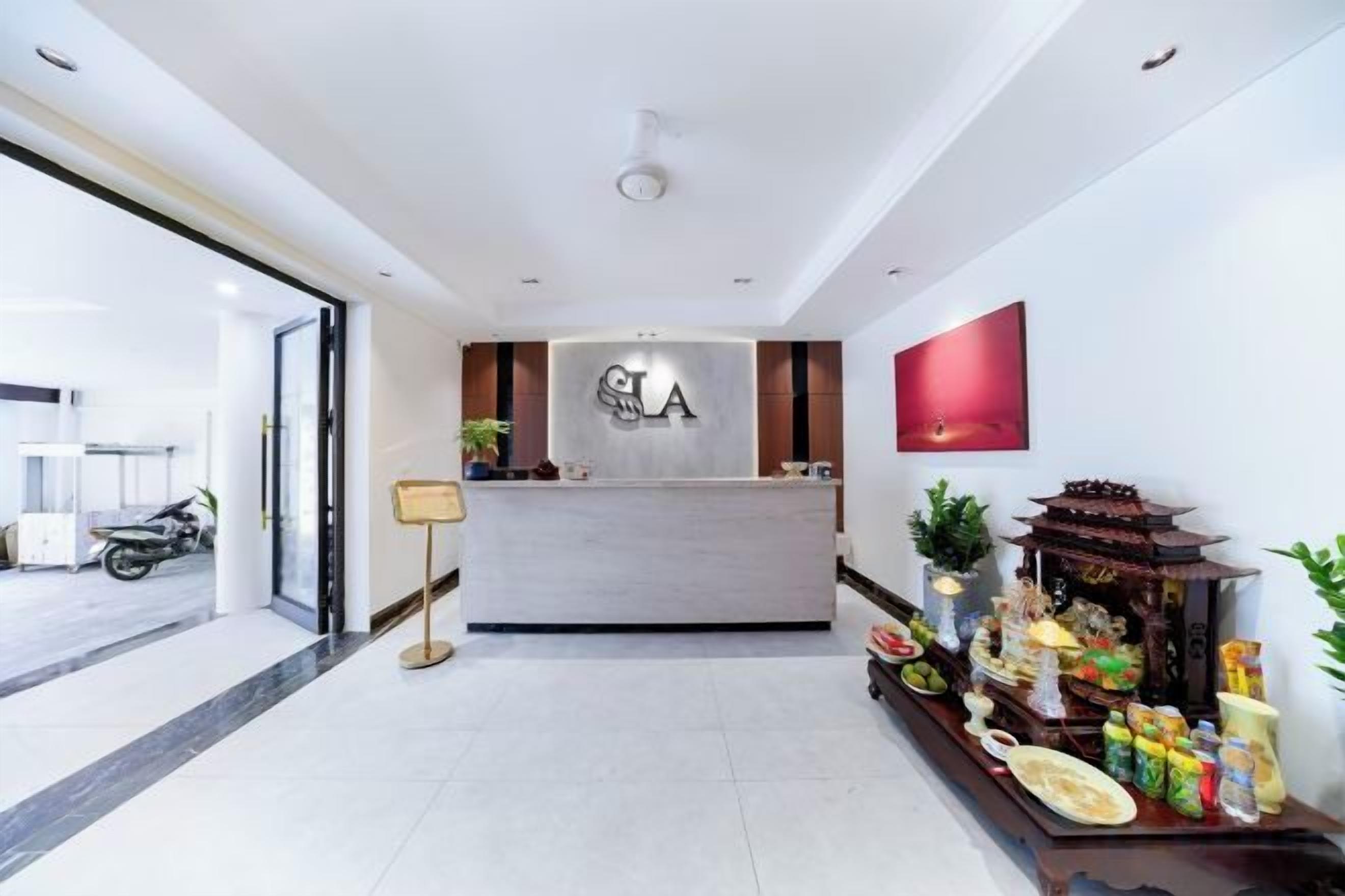 A hotel reception area with a reception desk, a wall-mounted TV, and a decorative altar with offerings.
