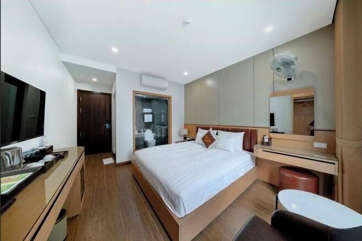 Une chambre d’hôtel moderne équipée d’un lit, d’un bureau, d’une télévision et d’une salle de bain visible à travers une porte ouverte.