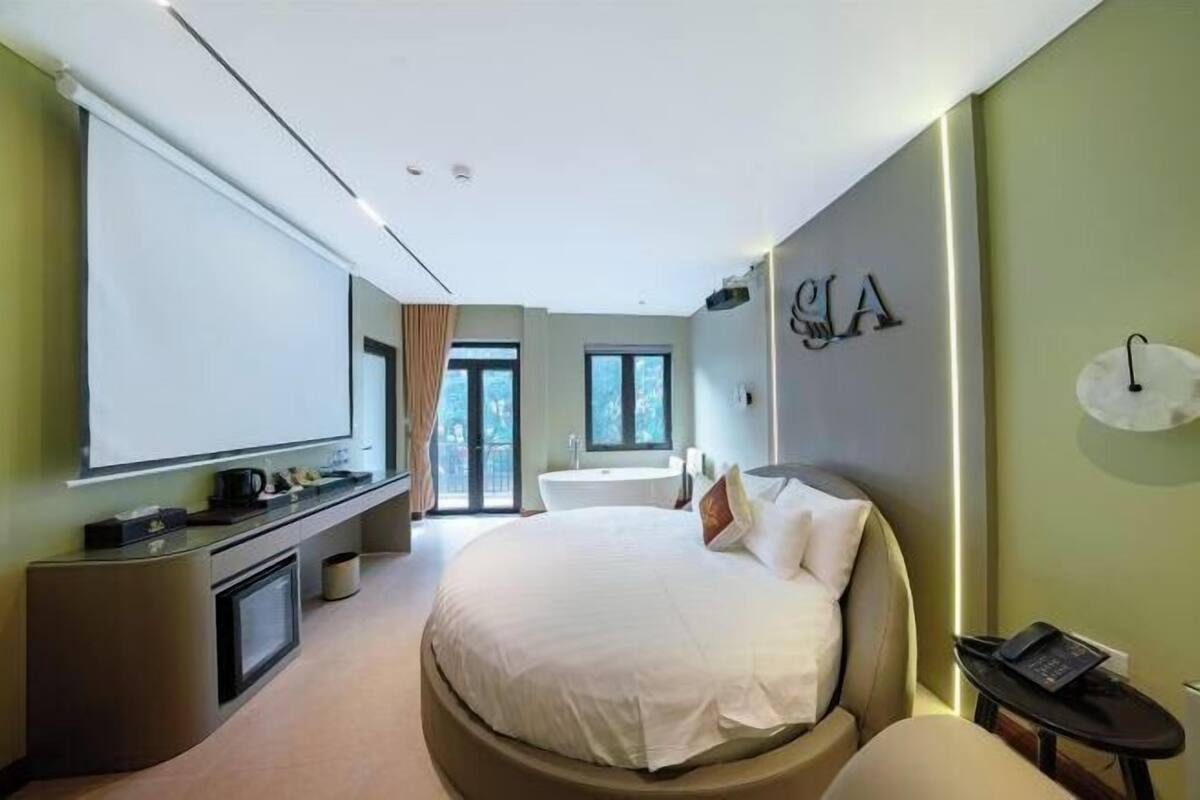Une chambre d’hôtel moderne dotée d’un grand lit, d’un bureau avec un téléviseur à écran plat, d’une salle de bain avec baignoire et d’une grande fenêtre.