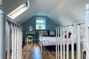 A bedroom with a sloped ceiling, a bed, a desk, and a window with a view.
