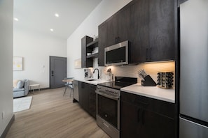 Une cuisine moderne avec des meubles de couleur sombre, des appareils en acier inoxydable et un plan de travail blanc.