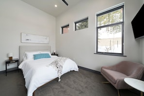 Une chambre moderne avec un grand lit, une table de chevet, une chaise et un téléviseur fixé au mur.