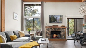 Una sala de estar con chimenea de piedra, un sofá gris y una zona de comedor con una mesa y sillas.