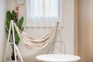 A room with a white round table, a beige hammock, and a large green plant with red flowers. - Cantabile Meidaimae (Tokyo)