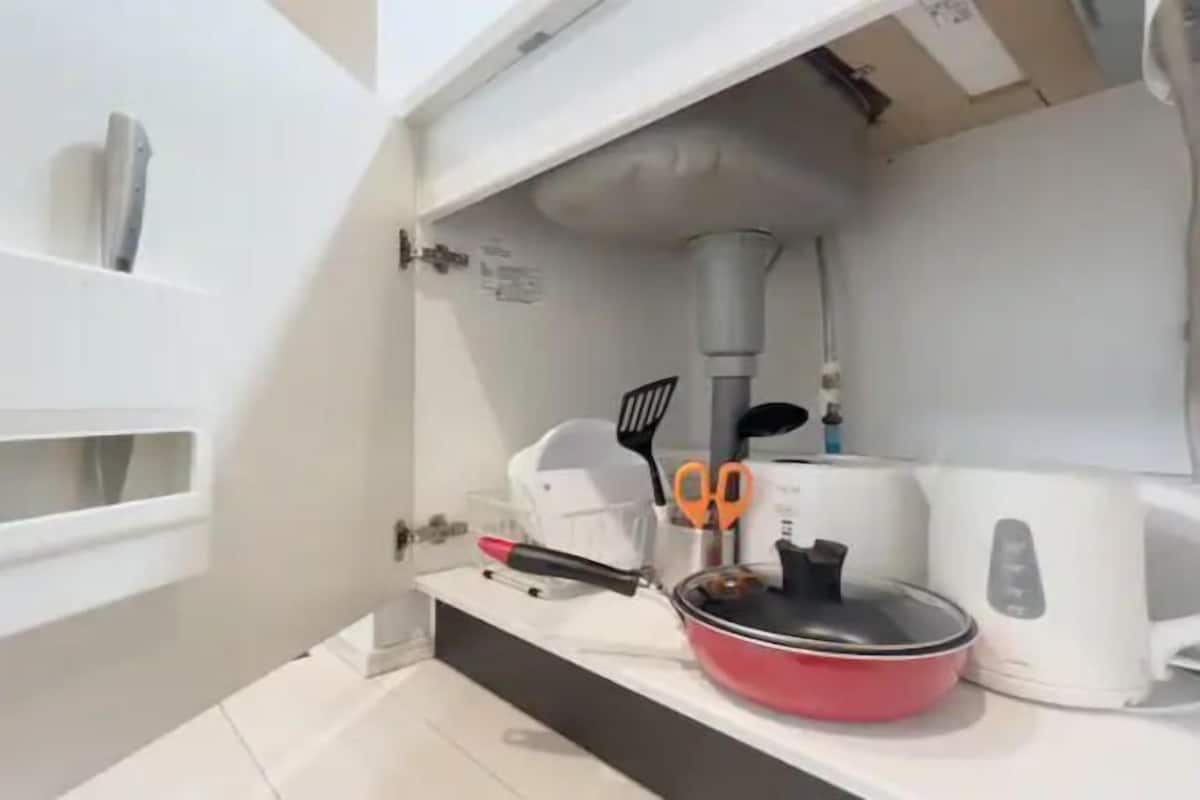A kitchen with a white countertop, a red pot, a kettle, and a pair of scissors.