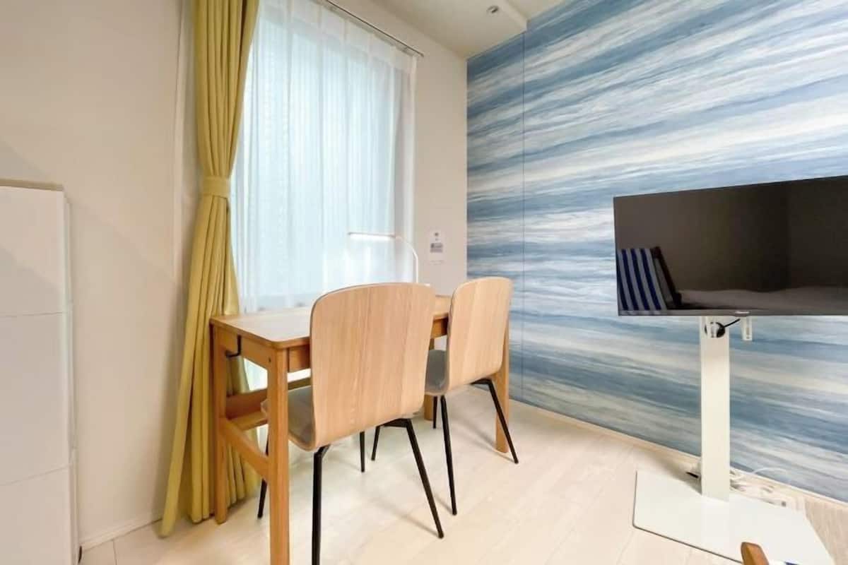 A modern dining area with a wooden table and chairs, a window with yellow curtains, and a wall with a blue and white abstract pattern.