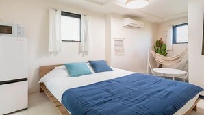 A bedroom with a bed, a small table, a chair, an air conditioning unit, and a window with curtains. - Cantabile Meidaimae (Tokyo)