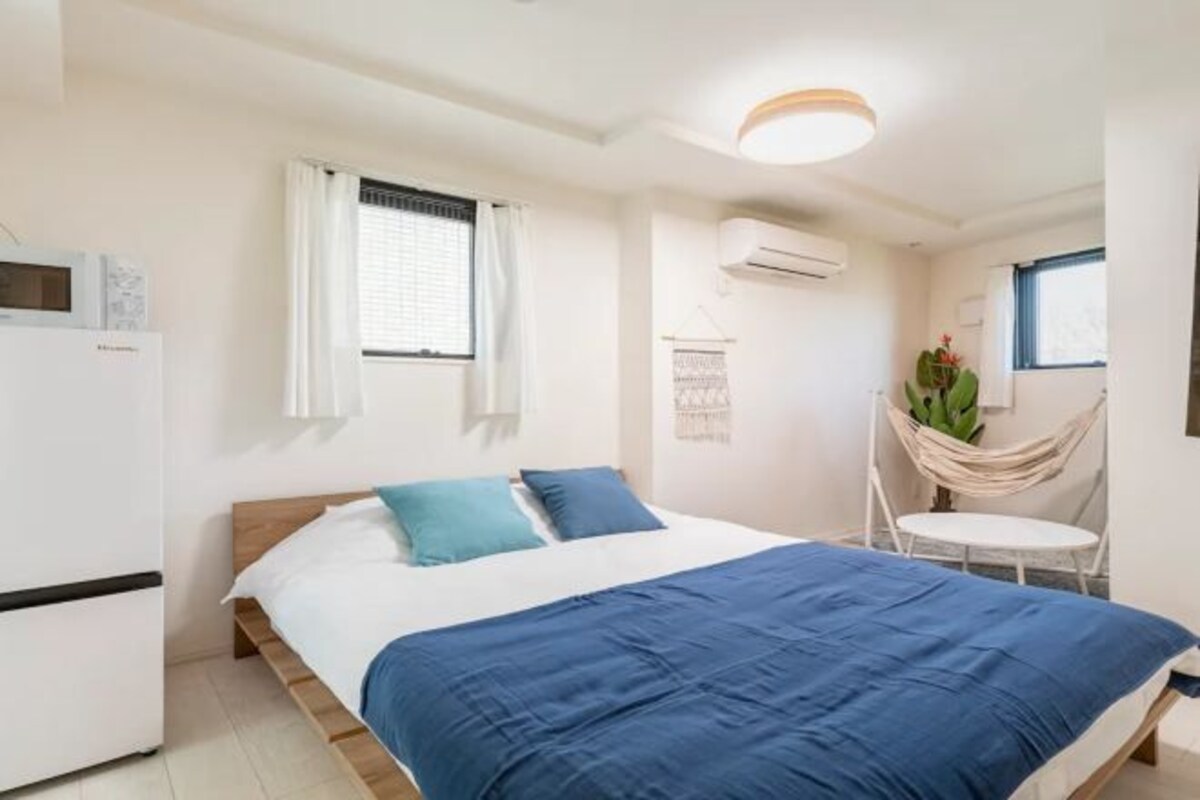 A bedroom with a bed, a small table, a chair, an air conditioning unit, and a window with curtains.
