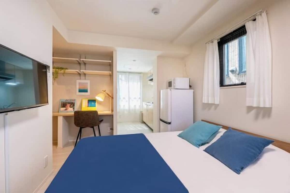 A bedroom with a bed, a desk, a chair, a TV, and a window with curtains.