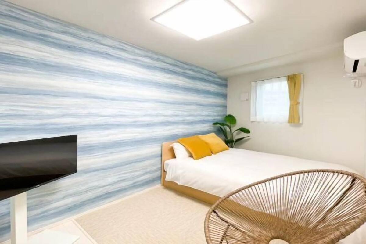 A bedroom with a bed, a TV, a plant, and a wall with a blue and white pattern.