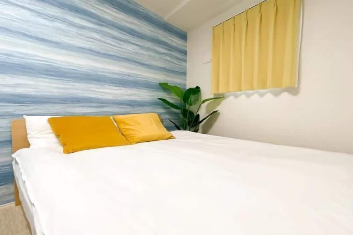 A bedroom with a bed, a yellow pillow, a plant, and a wall with a blue and white pattern.