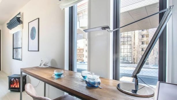 A modern room with a wooden desk, a chair, a table lamp, and a window with a view of buildings. - Cantabile Meidaimae (Tokyo)