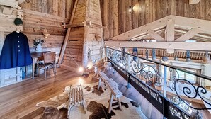 A rustic interior with wooden walls, a staircase, a dining area with a table and chairs, and a decorative railing.