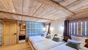 A wooden cabin bedroom with two beds, a built-in sink, and a window with curtains.
