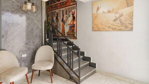 Een modern ontworpen trap, beklemd door twee stoelen en een kunstwerk aan de muur met afbeeldingen van oude Egyptische figuren.