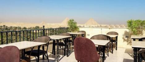 Une terrasse extérieure avec des tables et des chaises, d’où l’on peut admirer les pyramides au loin.