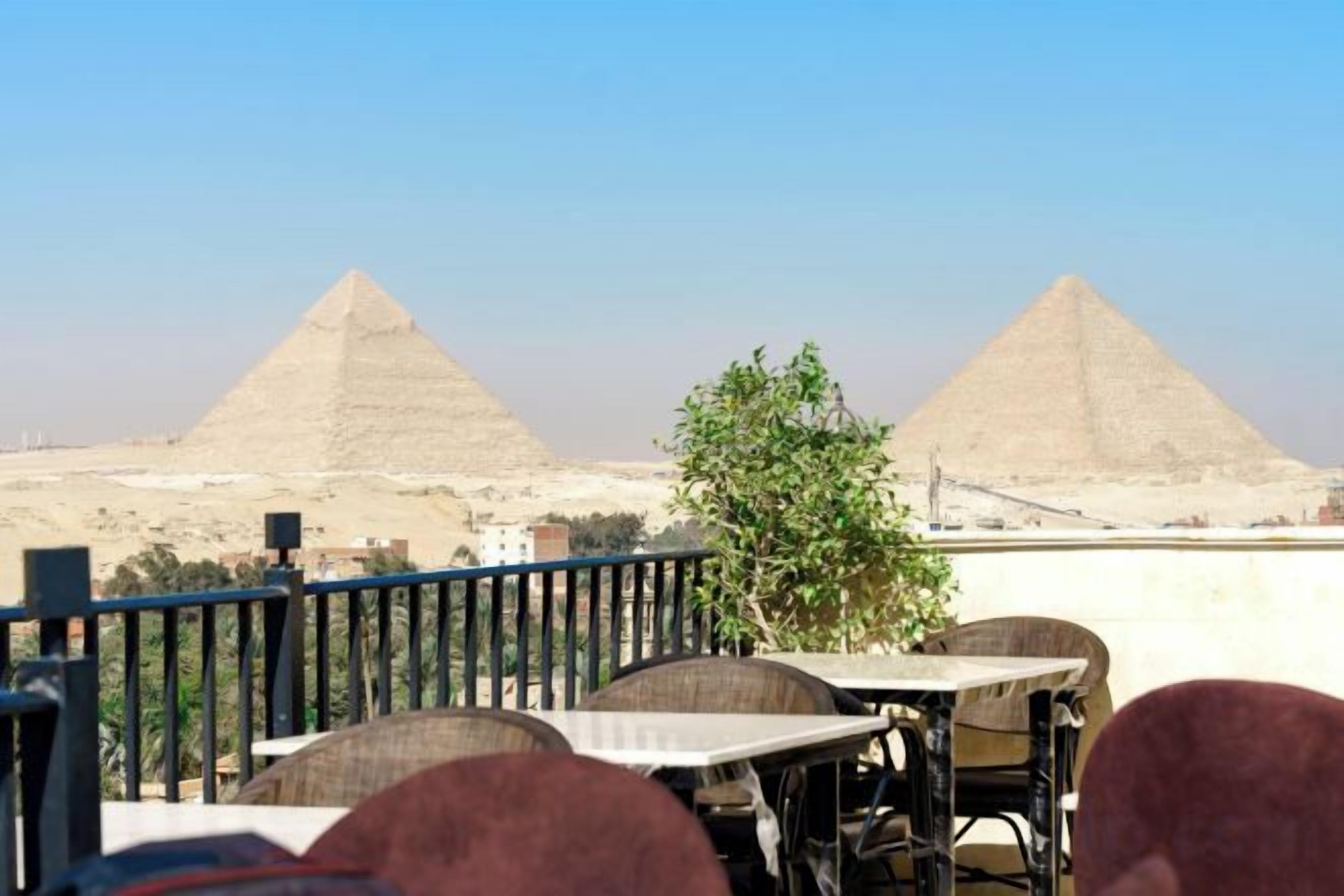 A dining area with tables and chairs, a railing, and views of two pyramids.