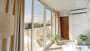 Een balkon met grote schuifdeuren, een plant in pot, een witte bank en een airconditioning.
