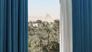 Uitzicht door gordijnen op een piramide, palmbomen en gebouwen in de verte.