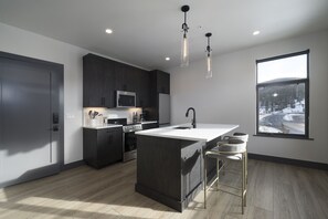 Une cuisine moderne avec des meubles de couleur sombre, un îlot central, un évier en acier inoxydable et une grande fenêtre donnant sur un paysage enneigé.