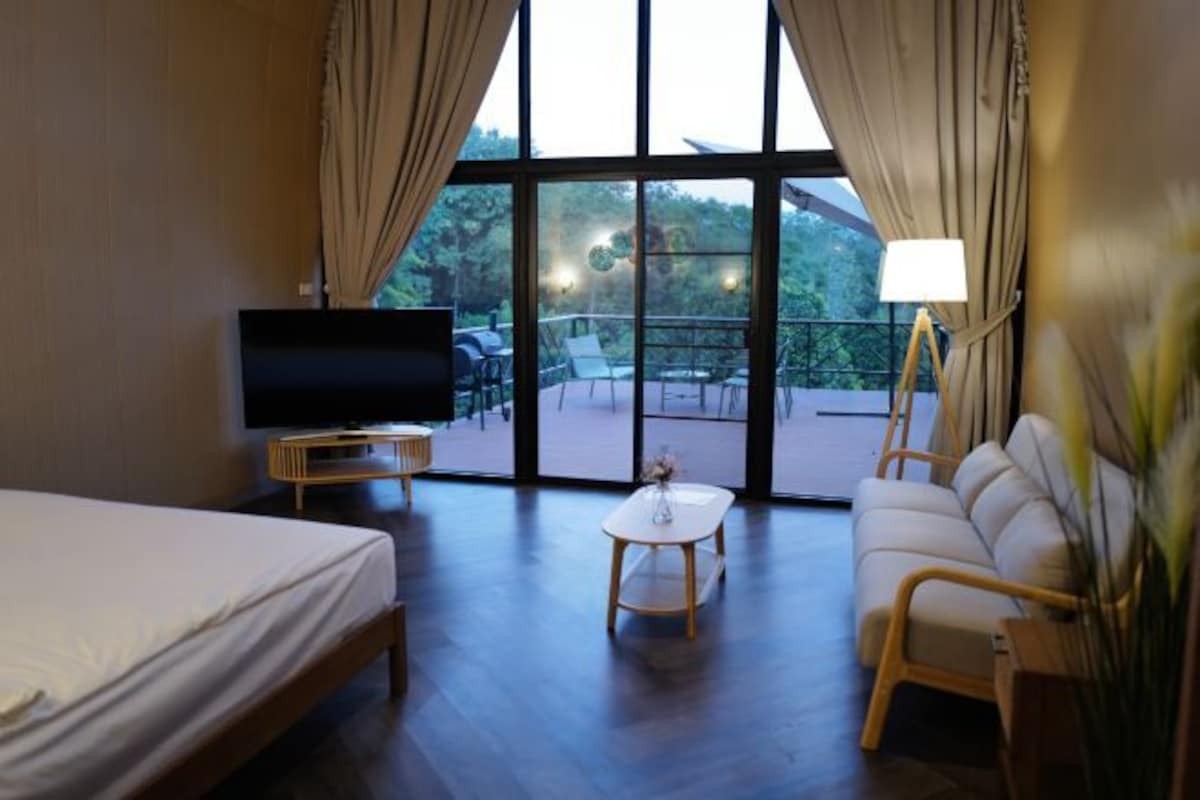 A hotel room with a bed, a TV, a small table, a sofa, and a balcony with outdoor furniture.