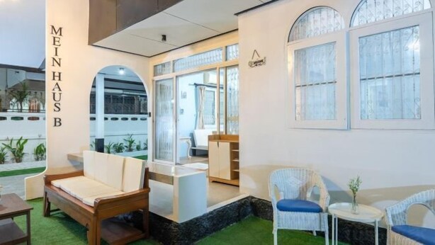 Un intérieur moderne avec un canapé, des fauteuils et une petite table. Une fenêtre offre une vue sur l’extérieur.