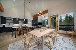 Une cuisine moderne avec des meubles de couleur sombre, une table à manger en bois et des luminaires suspendus.