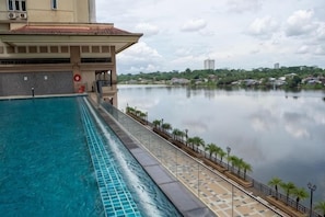 A swimming pool with a view of a calm lake, a building with a tiled roof, and a distant cityscape.