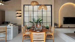 A modern dining area with a wooden table, wicker chairs, and a large window with a grid pattern. - MDF Villa Canggu (Bali)