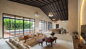 A spacious living area with a large window overlooking a pool, a seating area with a sofa and coffee table, and a dining area with chairs and a table. - MDF Villa Canggu (Bali)