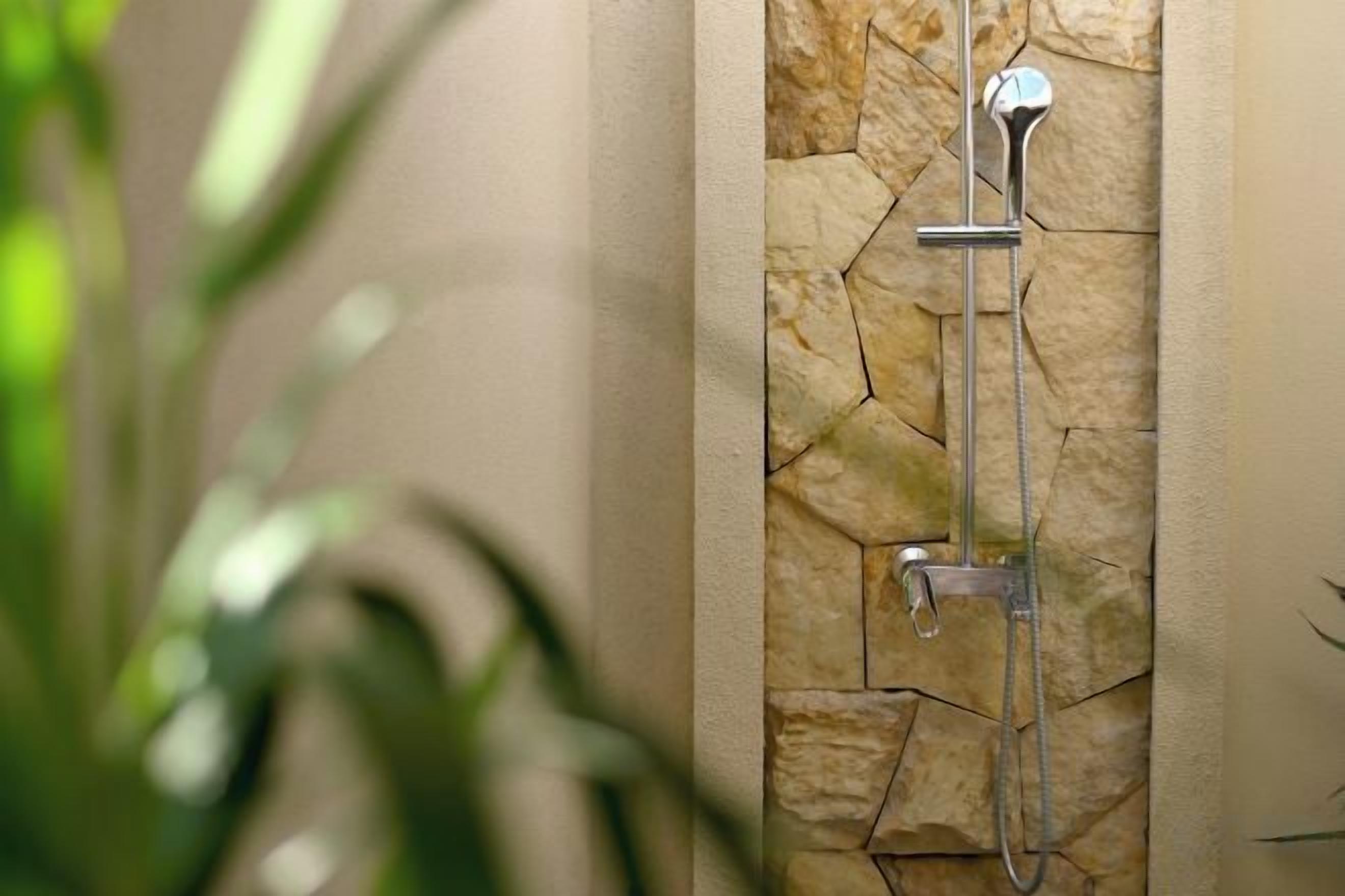 Een douche met een achtergrond van een stenen muur en een metalen douchekop.