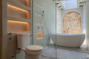 A modern bathroom with a freestanding bathtub, a toilet, and a stone wall. - MDF Villa Canggu (Bali)