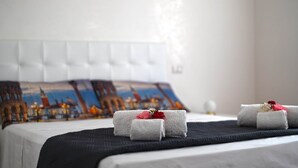 A neatly made bed with a black bedspread, a white headboard, and a pillow with a cityscape design.