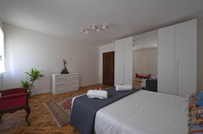 A bedroom with a bed, a dresser, a mirror, a red chair, and a potted plant.