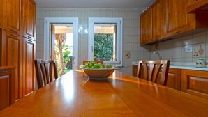 A wooden dining table with chairs, a bowl of fruit, and wooden cabinets in a kitchen.