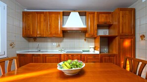 A kitchen with wooden cabinets, a white countertop, and a dining table with a fruit bowl.