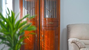 A wooden wardrobe with glass panels and a brass handle, a beige armchair, and a potted plant.
