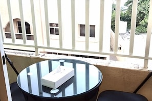 En balkon med et rundt glasbord, en hvid kasse og en sort stol.
