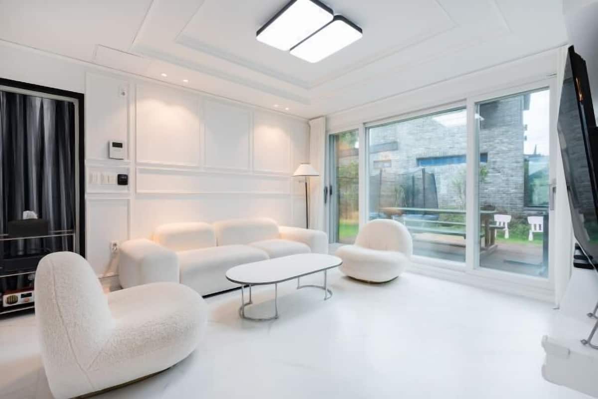 A modern living room with a white sofa set, a coffee table, and a large sliding glass door leading to a balcony.