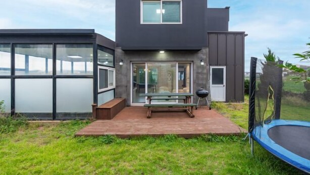 Ein modernes Haus mit Terrasse, Tisch und Trampolin.