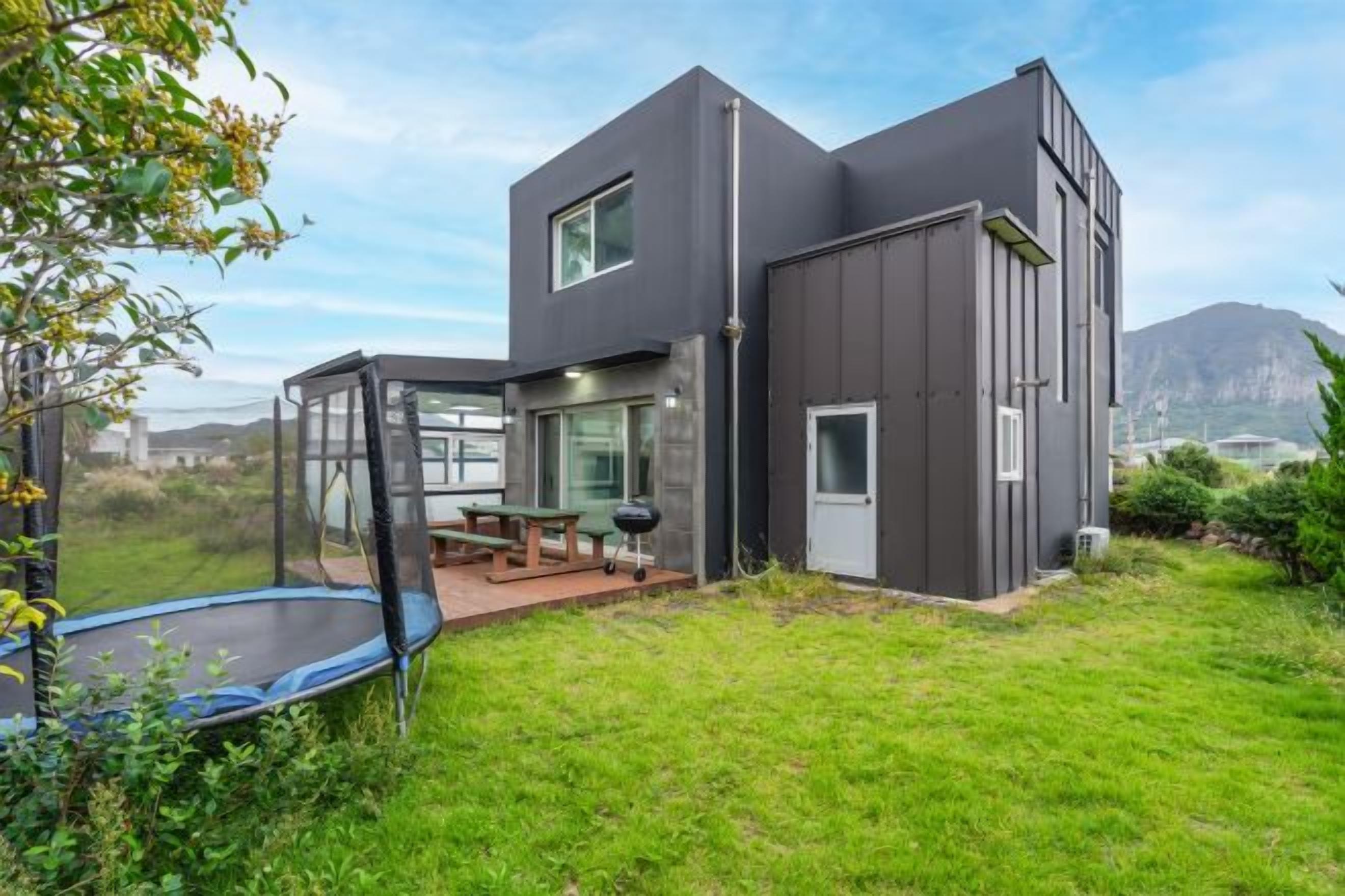 A modern two-story house with a covered patio, a trampoline, and a view of the mountains.