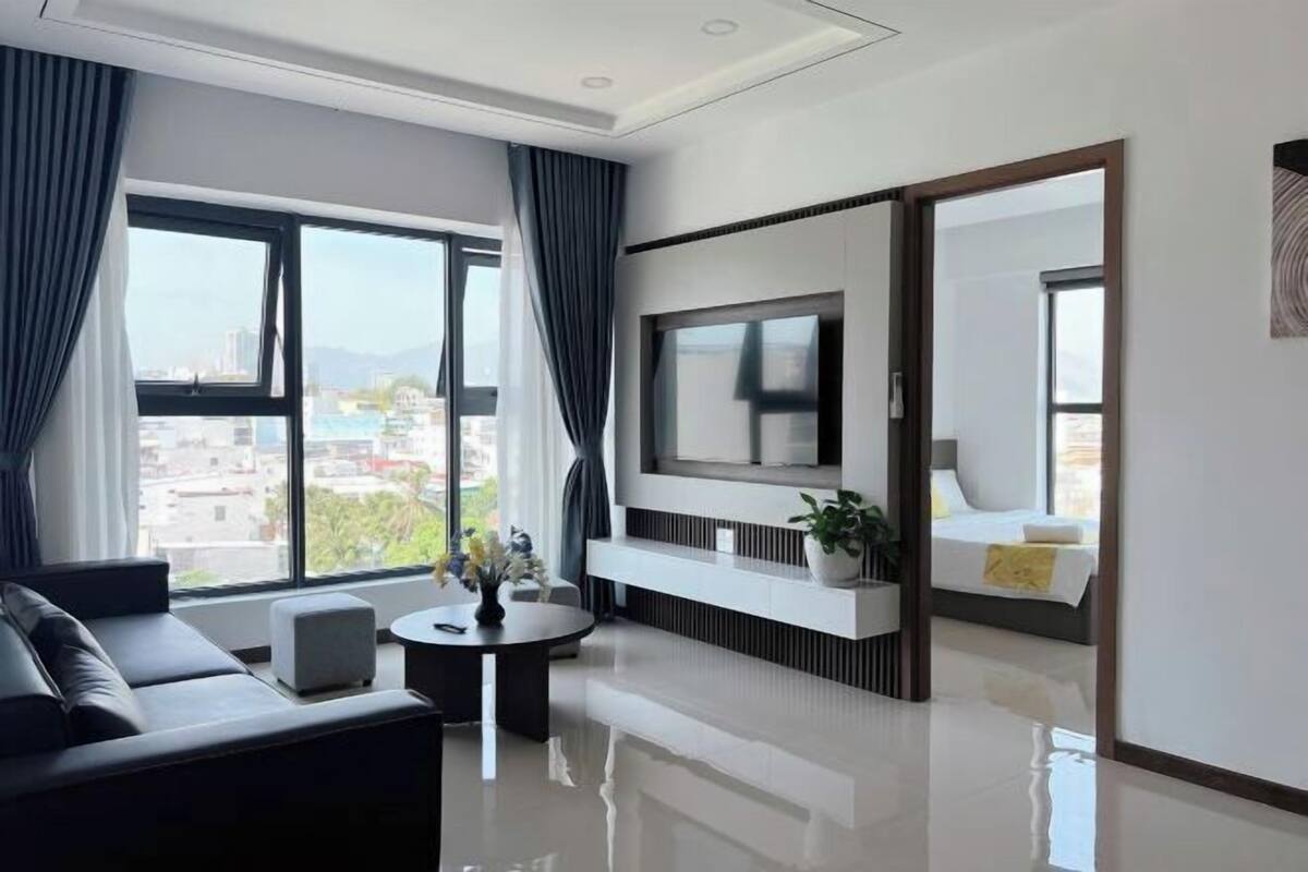 Une chambre d’hôtel moderne dotée d’une grande fenêtre, d’un téléviseur à écran plat, d’un canapé, d’une petite table et d’une plante en pot.
