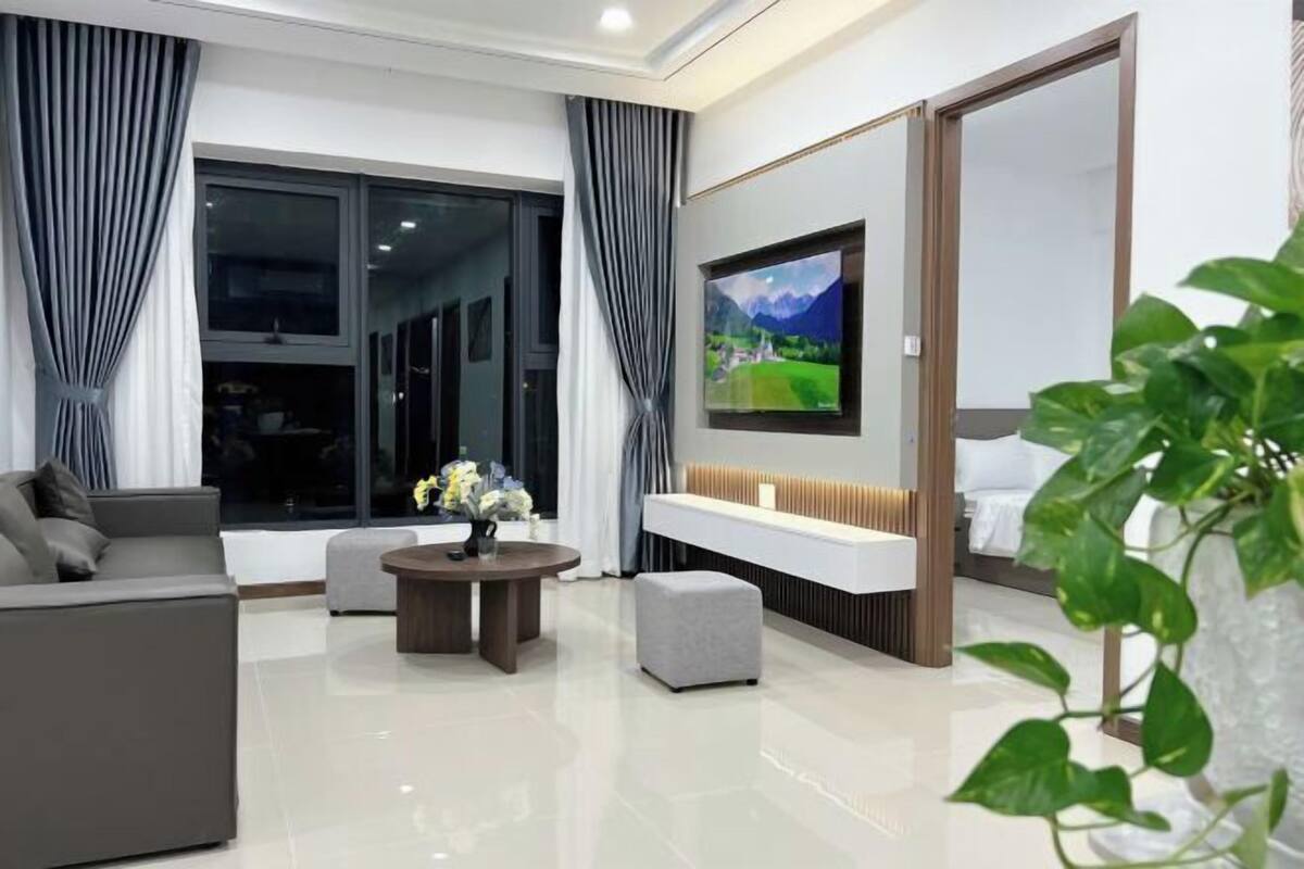 Un salon moderne avec un canapé, une table basse, un téléviseur fixé au mur et une plante.