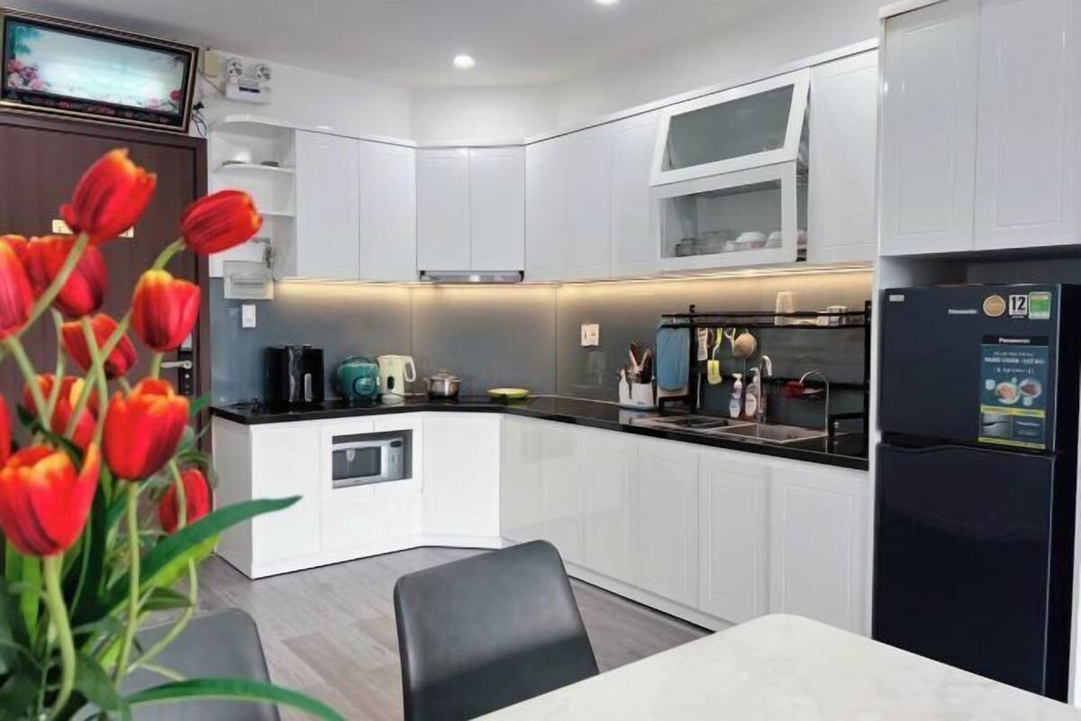 Une cuisine moderne avec des meubles blancs, un réfrigérateur noir et un coin repas comprenant une table et des chaises.